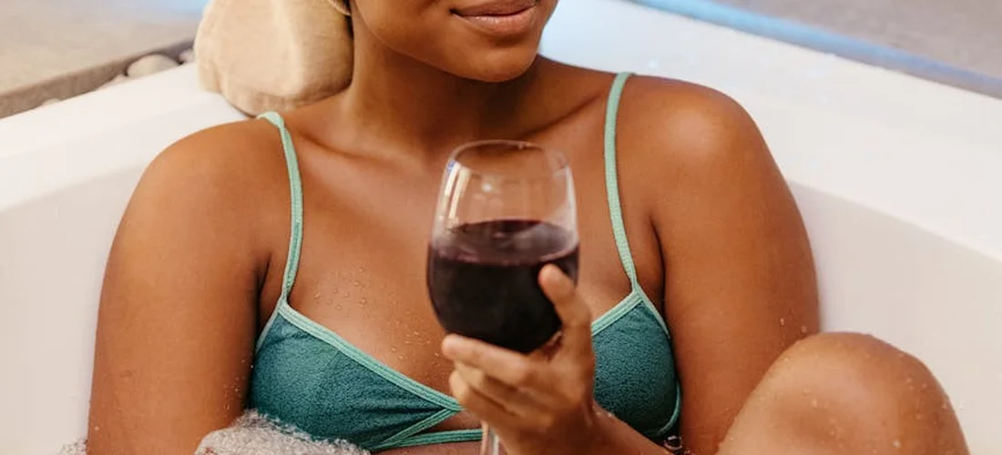Person in a teal bikini relaxing in a hot tub, holding a glass of red wine