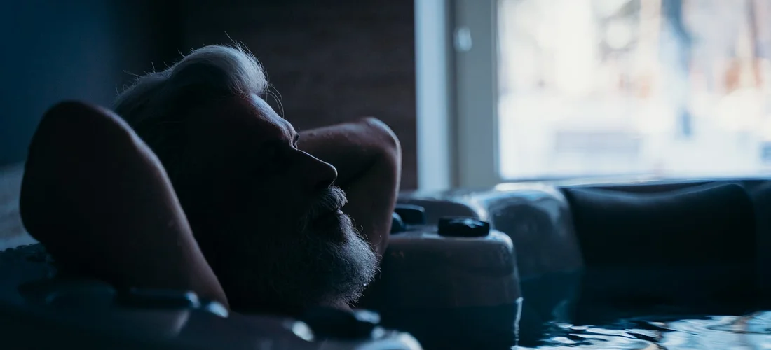 A person relaxing in a dimly lit hot tub, leaning back as jets circulate the water.