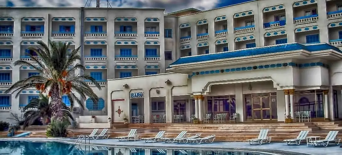 Outdoor hotel pool area with lounge chairs and a multi-story building in the background