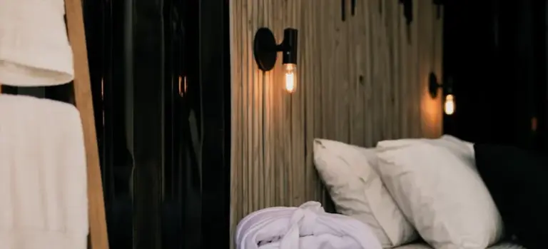 Hotel bedroom scene with a white robe on the bed, pillows, and warm wall lights