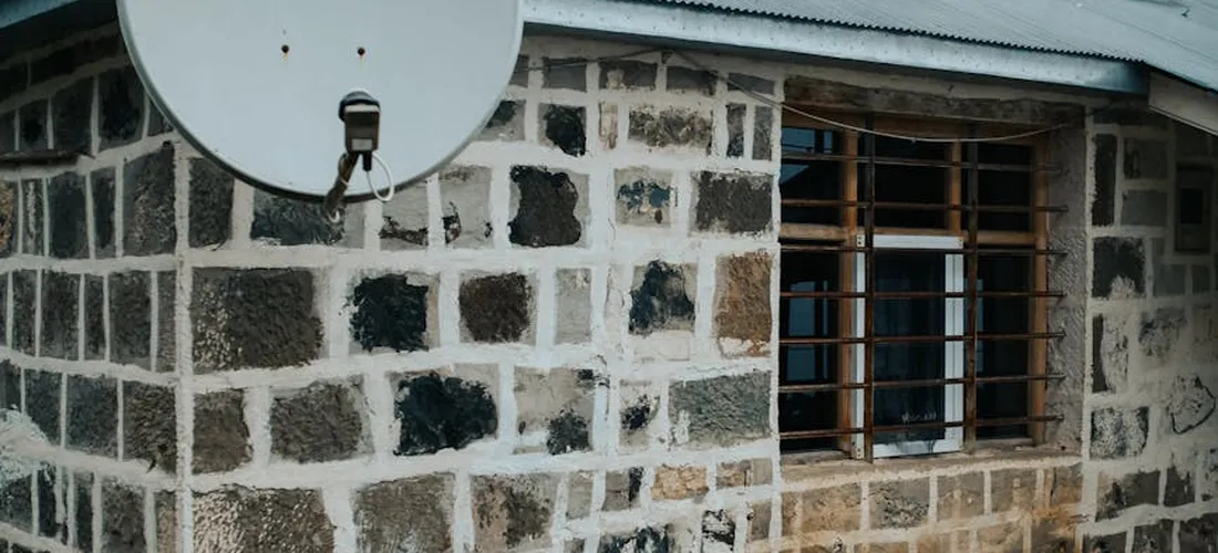 Stone exterior wall with a satellite dish and a window with bars