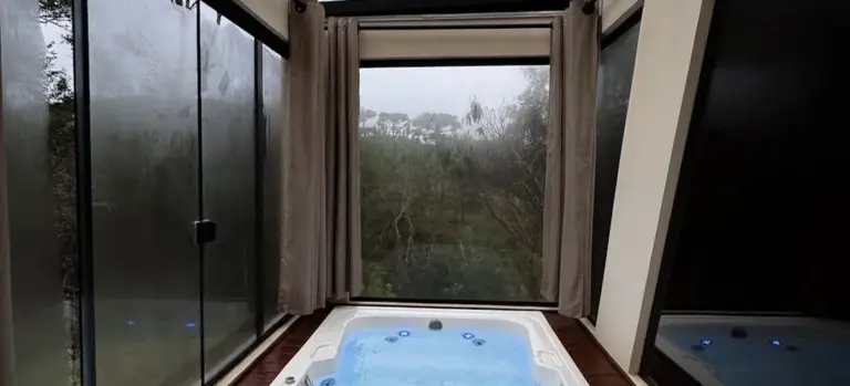 Indoor hot tub with blue water in a sunroom, flanked by glass walls and beige curtains