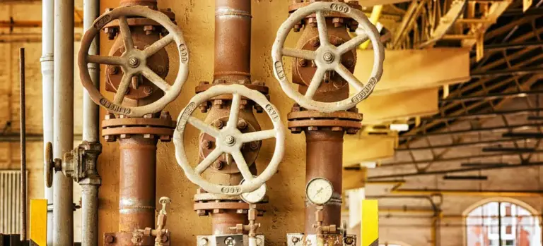 Three large wheel valves on rusted vertical pipes in an industrial setting.