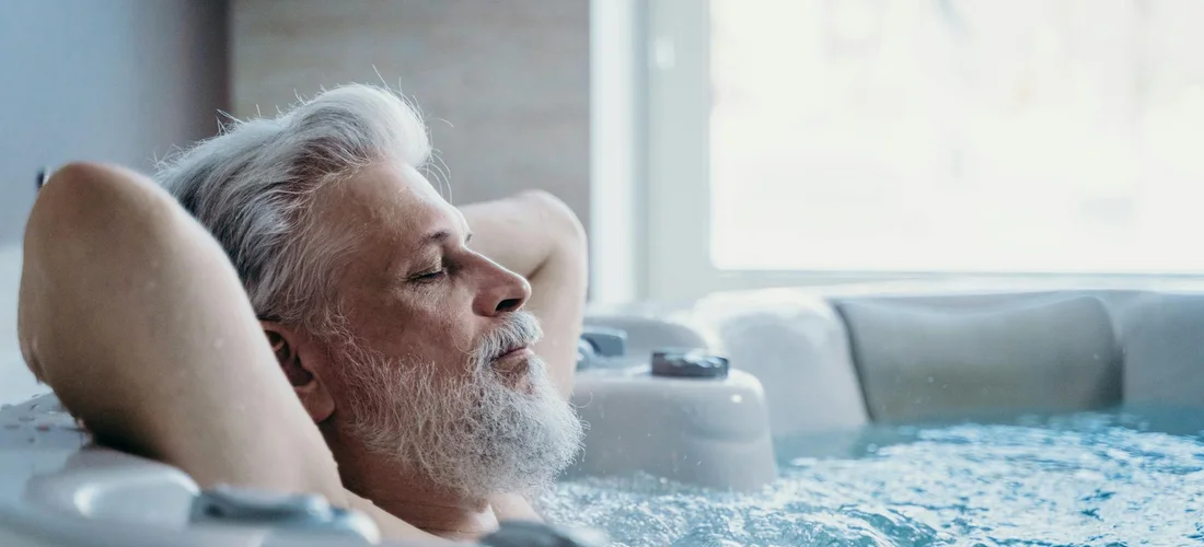 Older man with white hair and beard relaxing in a Jacuzzi tub with jets