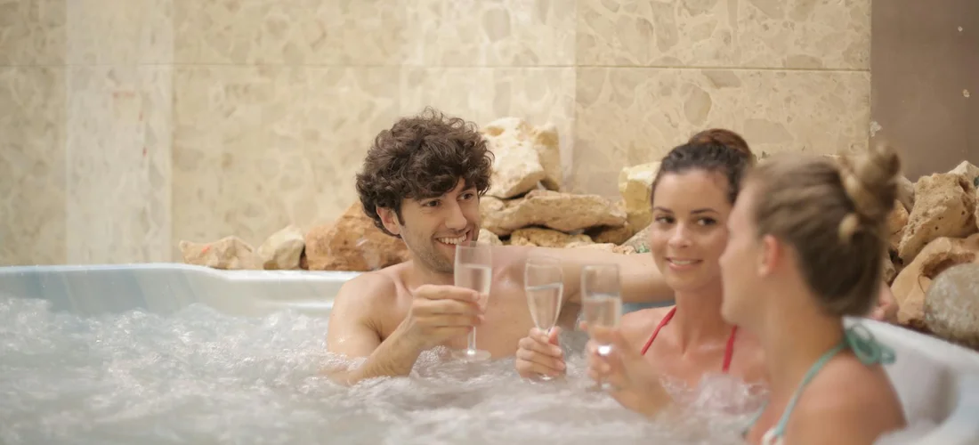 Group of people relaxing in a Jacuzzi tub with jets, holding drinks