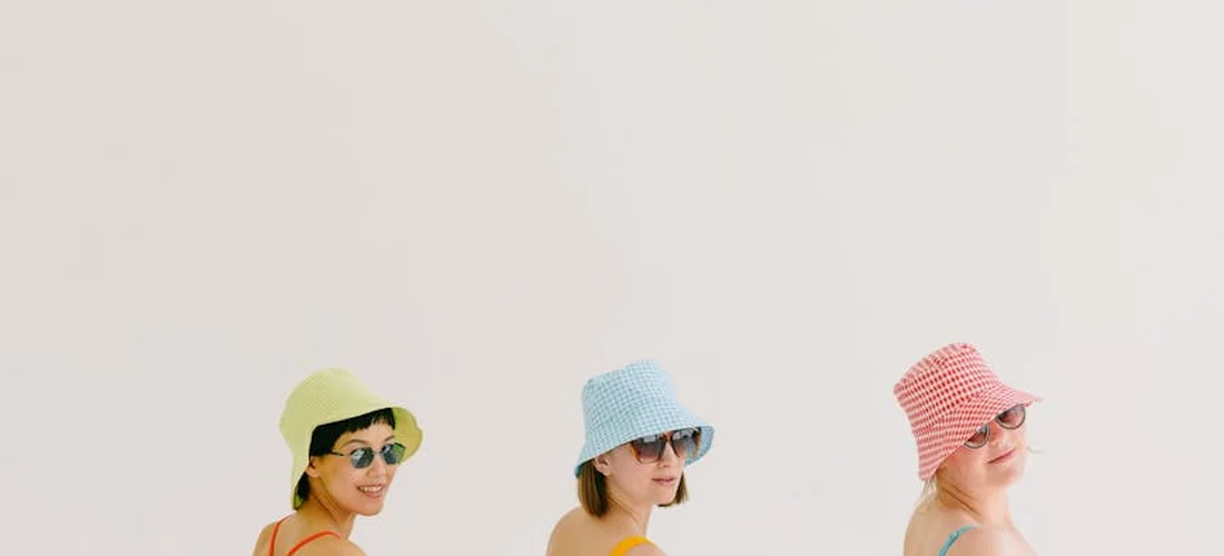 Three women wearing wide-brimmed hats and sunglasses, posing against a pale background.