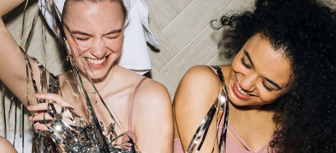 Two smiling women in a bathroom with glass shards around them, illustrating the practical realities of bathroom renovations.