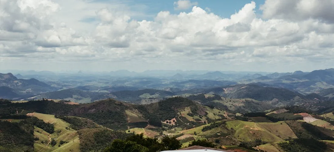 Wide landscape view of rolling green hills and distant mountains under a partly cloudy sky.