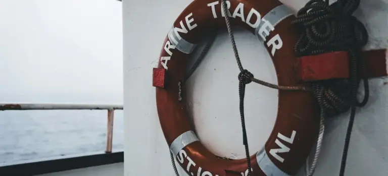Lifebuoy ring with rope hanging on a boat rail with the sea in the background.
