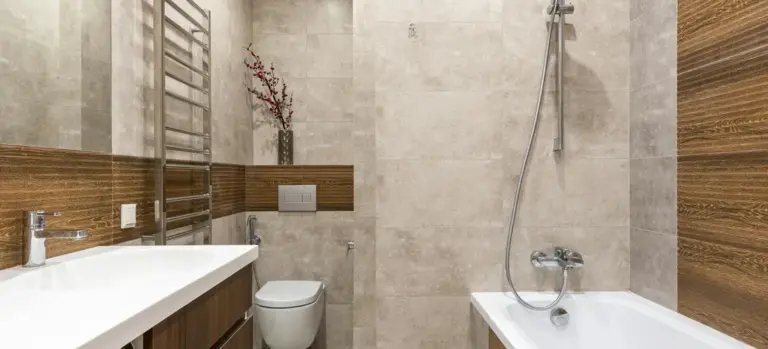 A contemporary bathroom featuring a white bathtub with a handheld showerhead, a wall-mounted toilet, a long wooden vanity, and a metal towel warmer.