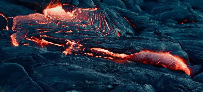 Close-up of glowing molten lava flowing over dark rocks.