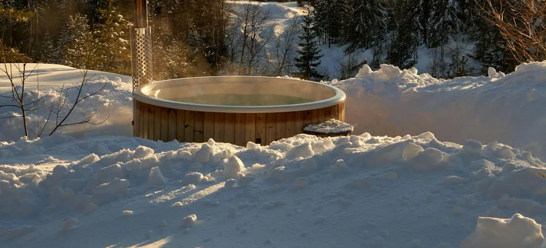 Outdoor wooden hot tub surrounded by deep snow in a winter landscape.