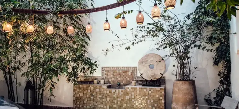 Outdoor courtyard with hanging lanterns, greenery, and a tile mosaic water feature