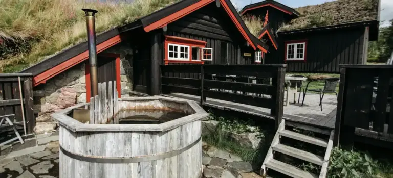 Rustic outdoor barrel-style hot tub with a wood deck and black wooden cabins in the background