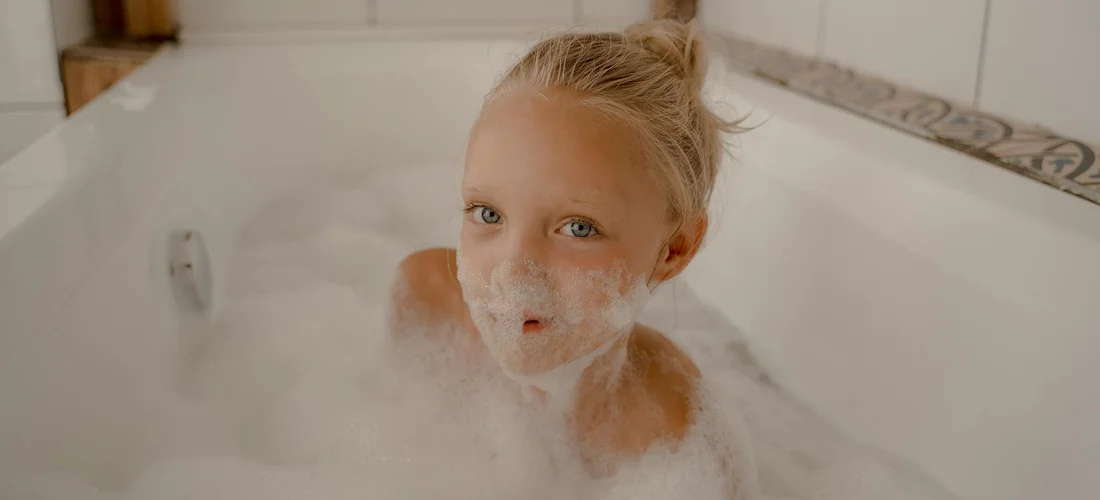 Person surrounded by bubbles in a bathtub, looking at the camera