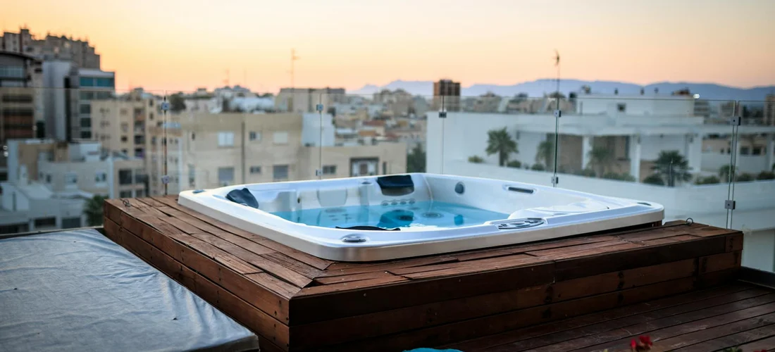 Rooftop deck with a rectangular jacuzzi hot tub overlooking a cityscape at sunset.