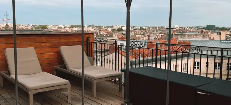 Rooftop terrace with two beige lounge chairs and a city skyline in the background.