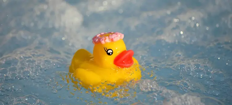 Yellow rubber duck floating in bubbly blue water of a hot tub