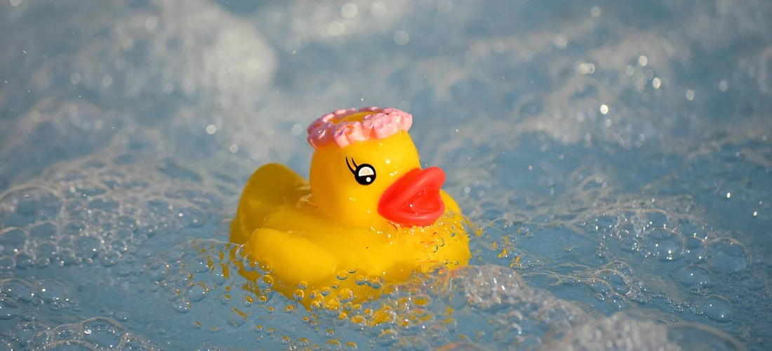 Yellow rubber duck floating in bubbly blue water of a hot tub