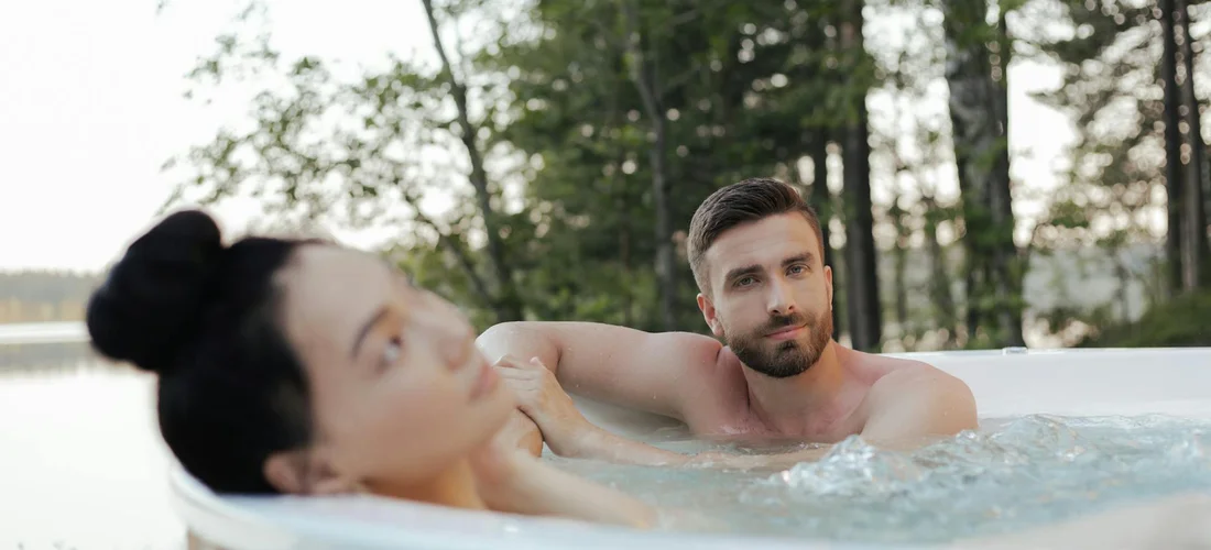 Two adults relaxing in an outdoor saltwater hot tub with greenery in the background