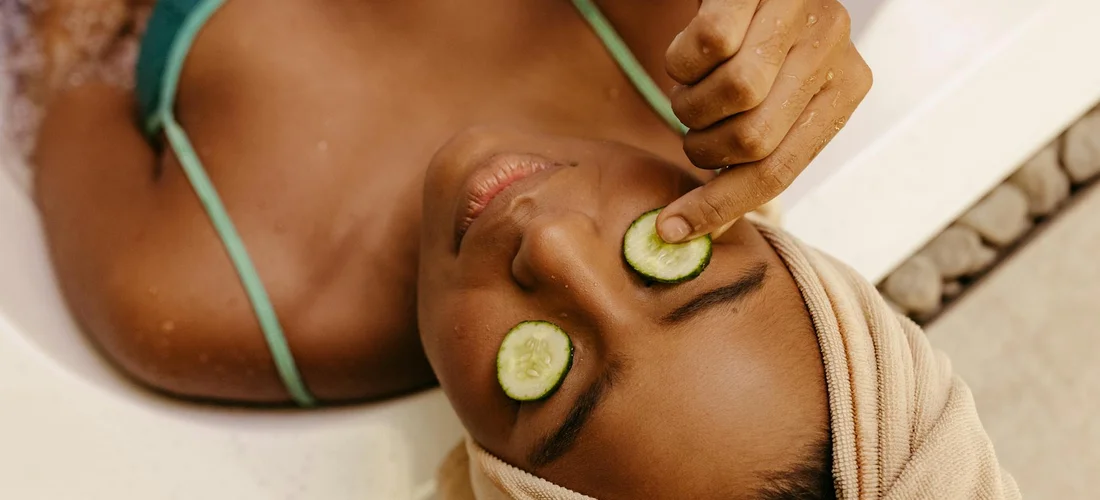 Woman relaxing in a hot tub with cucumber slices over her eyes and a towel wrapped around her head.
