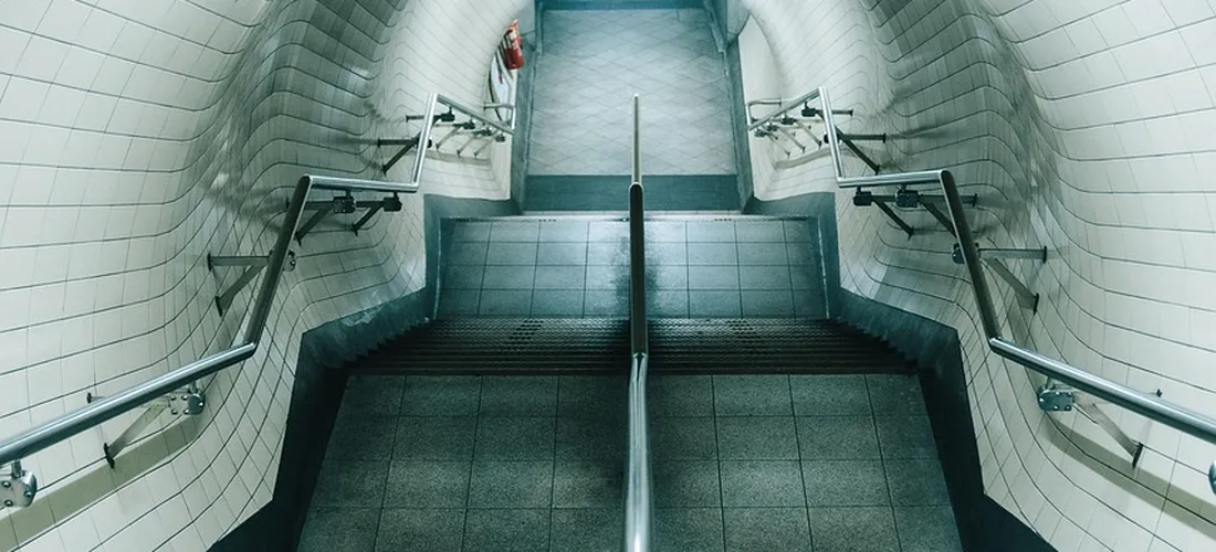 Tiled stairwell with metal handrails on both sides and a central barrier, showcasing a sturdy grip surface for safe use.