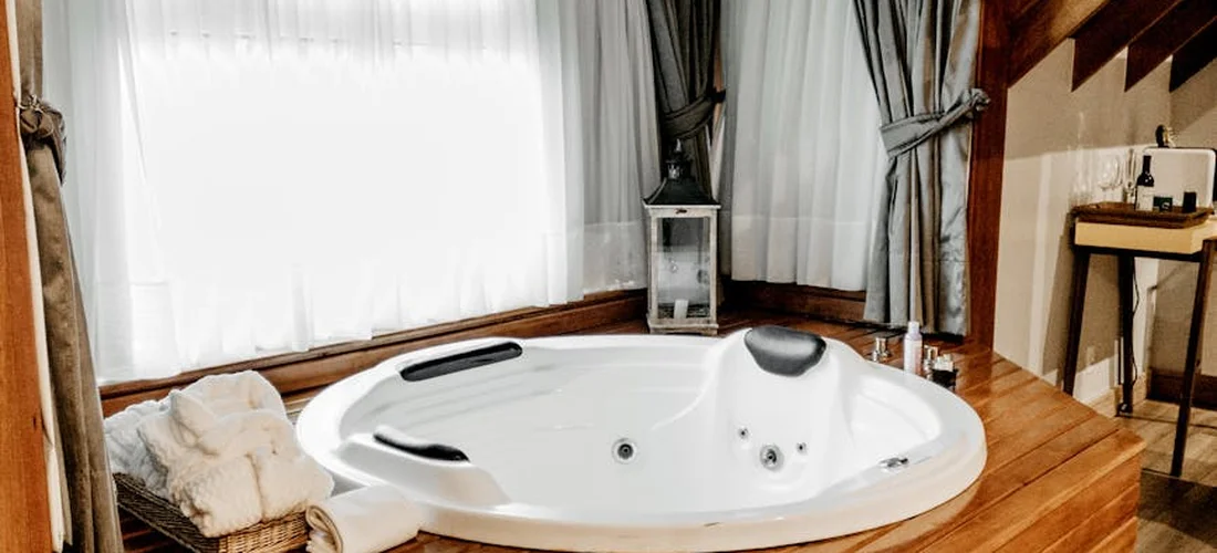 Round white hot tub in a wood-floored room with curtains, empty of people