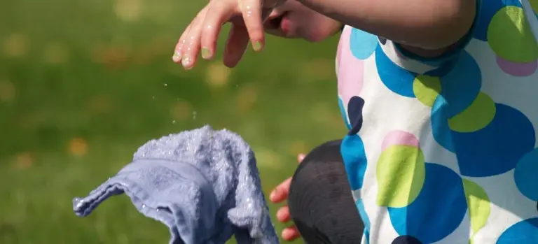A person wearing a colorful polka-dot shirt outdoors, reaching toward a towel with a grassy background.
