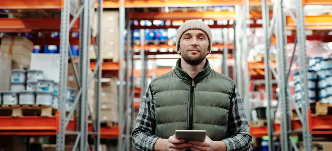 Warehouse worker in a storage facility aisle, holding a tablet and checking inventory.