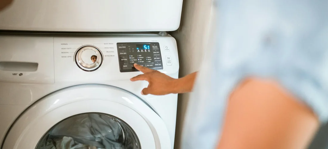 Person's hand pressing the control panel on a front-loading washing machine