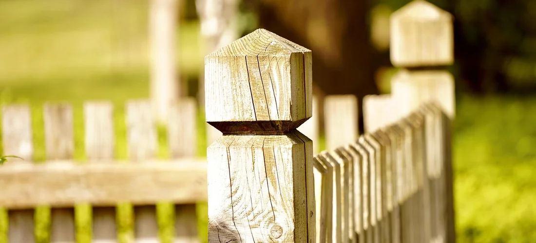 Close-up of a wooden privacy fence post with a sunlit, blurred background.